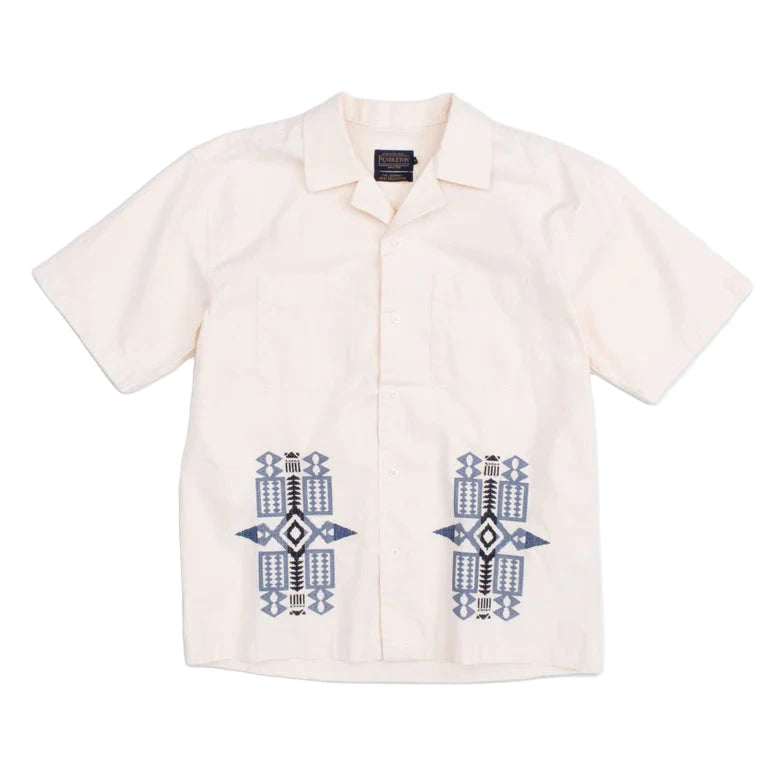 A beige camp collar shirt with blue geometric patterned needlework detail on the pockets.