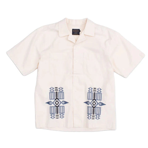 A beige camp collar shirt with blue geometric patterned needlework detail on the pockets.